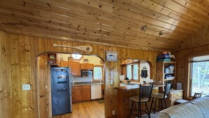 Interno di una baita in legno con angolo cottura, zona pranzo e soggiorno con divano.
