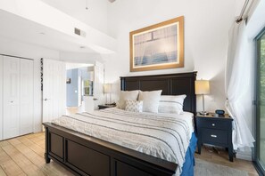 A bedroom with a large bed, a nightstand with a lamp, a framed picture on the wall, and a view of the outdoors through a window. - Vacay Getaway - Condo for 8 (Branson)
