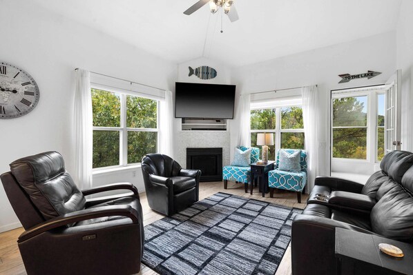 A modern living room with leather sofas, a flat-screen TV, a fireplace, and large windows offering a view of the outdoors. - Vacay Getaway - Condo for 8 (Branson)