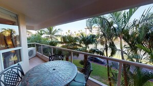 Ein Balkon mit rundem Tisch und Stühlen, der auf eine Straße mit Palmen und einem klaren Himmel blickt.