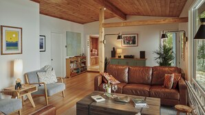 A spacious living room with a brown leather sofa, a wooden coffee table, and a bookshelf. - Private lakeside hideaway, 4 bedroom one-story home with stunning water views. (Sebago)