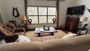 A living room with a sofa, a coffee table, a television, and a window with curtains.