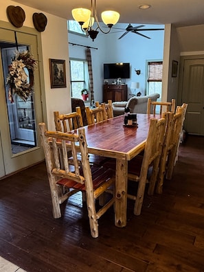 A dining area with a wooden table and chairs, a chandelier, and a ceiling fan.