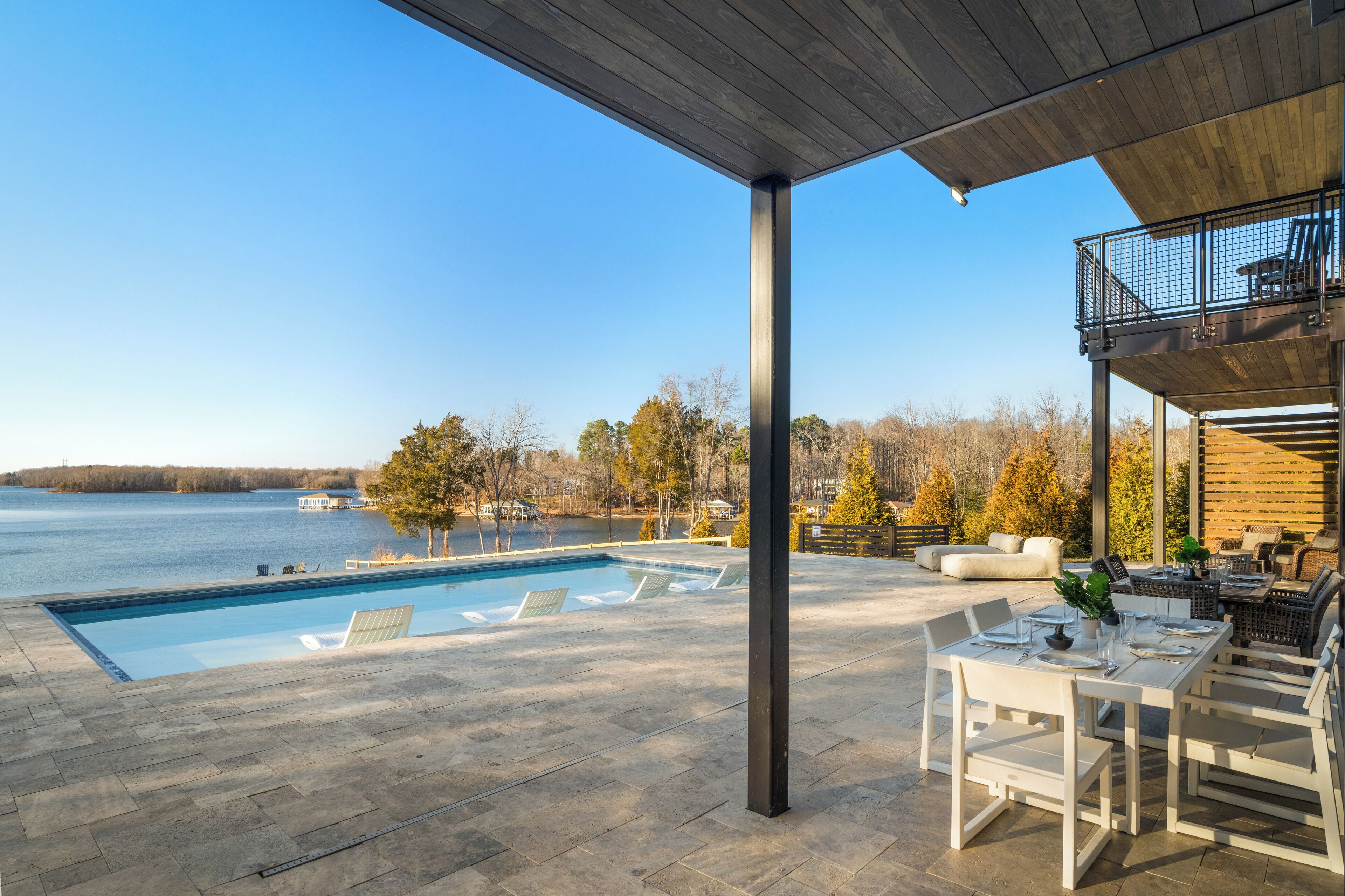 A pool area with a view of a lake, outdoor seating, and a covered patio.