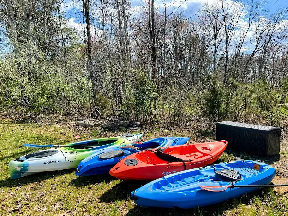 Des kayaks sont alignés sur l’herbe, avec des arbres en arrière-plan.