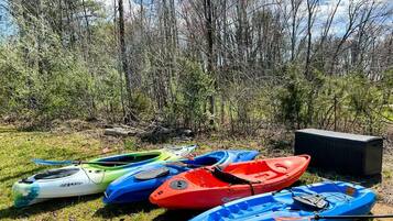 Des kayaks sont alignés sur l’herbe, avec des arbres en arrière-plan.