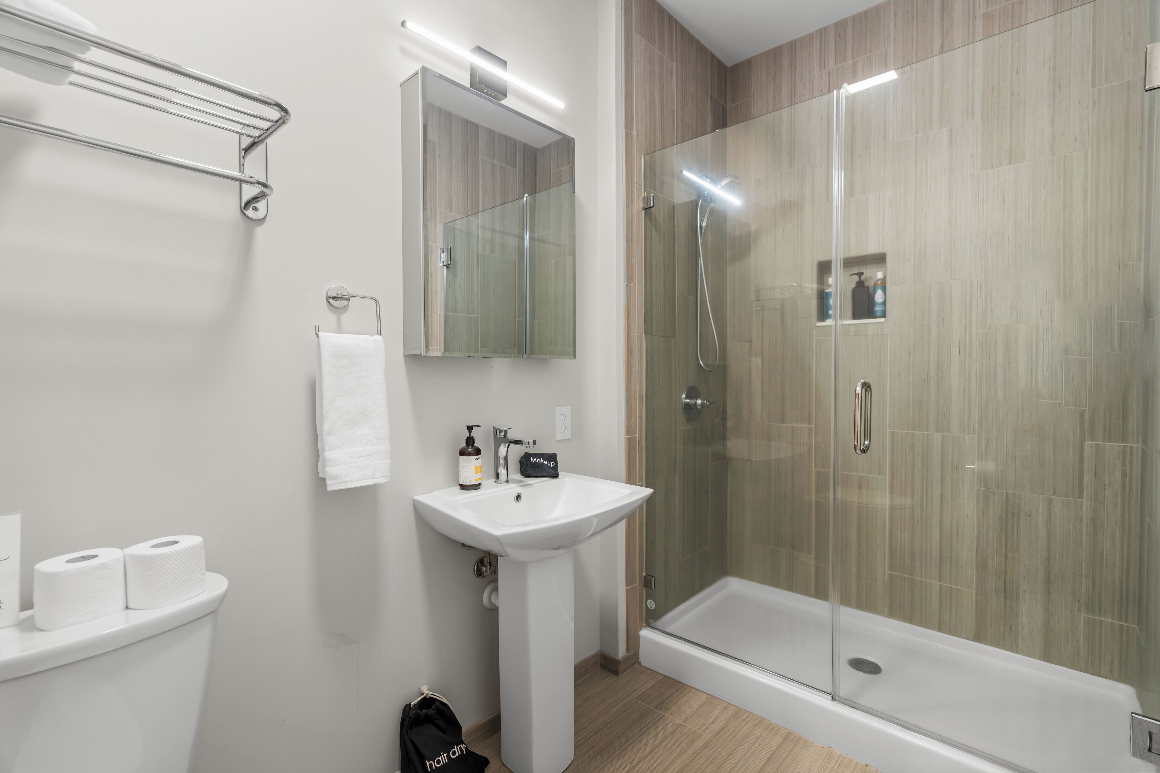 Un baño moderno con ducha de vidrio, un lavamanos blanco y un espejo encima.