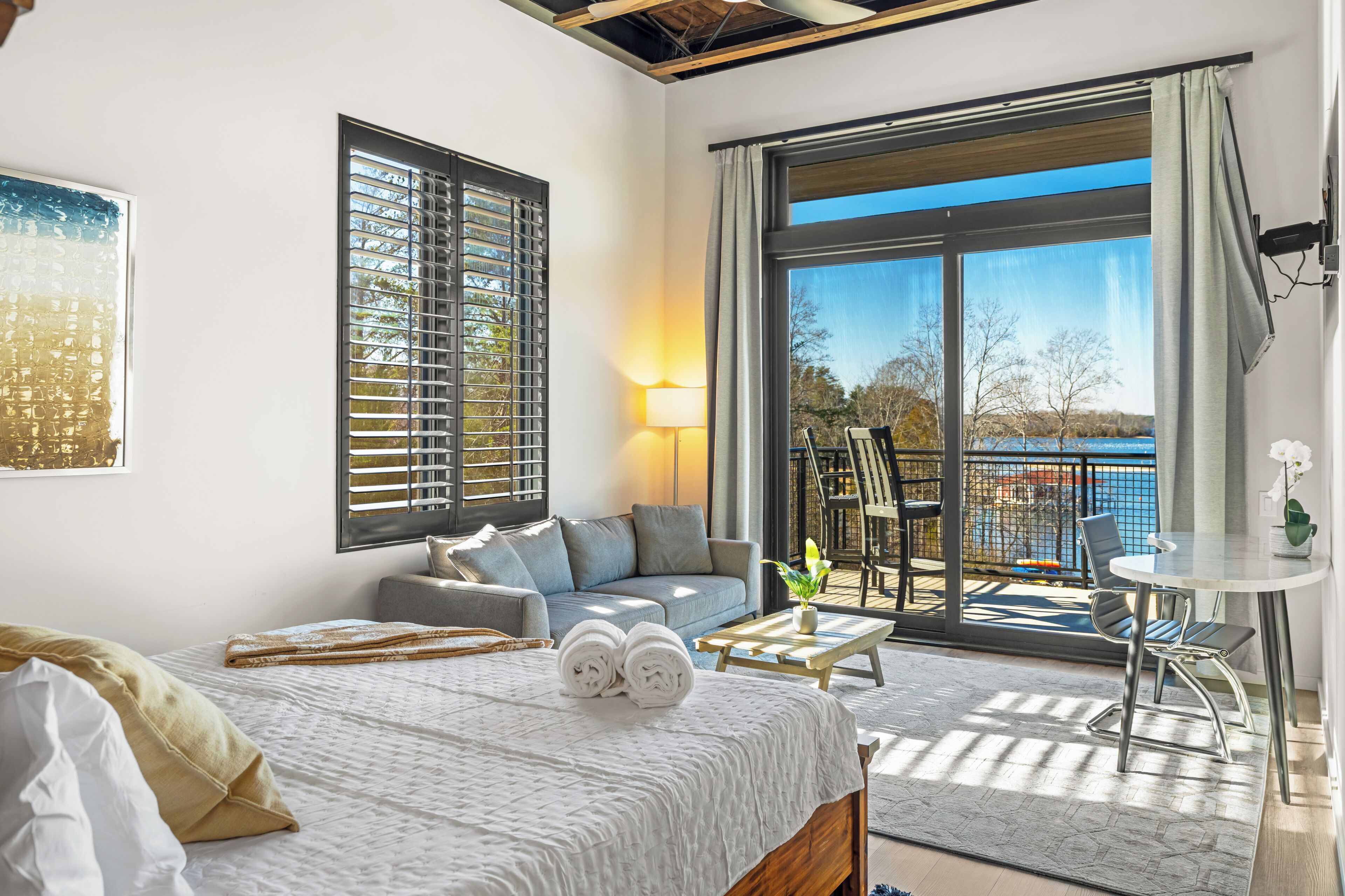 A bedroom with a bed, a sofa, a small table, and a balcony with a view of the sea.