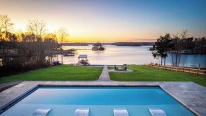 Une piscine avec des chaises longues, un quai et une vue sur un lac au coucher du soleil.