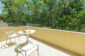 A balcony with a round table and two chairs, overlooking a lush green area with trees and a clear sky. - Paramar Viva Tulum by The Spot Rentals (Tulum)