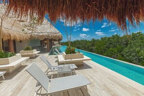 Une piscine à débordement offrant une vue imprenable sur l’océan, entourée de chaises longues et d’une structure à toit de chaume.