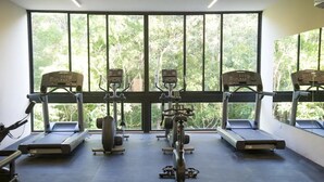 Una palestra con tapis roulant, ellittiche e macchinari per pesi, ampie finestre che danno su alberi.