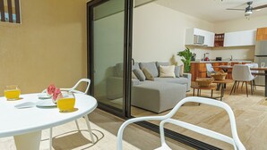 Un'area living moderna con divano, tavolo da pranzo e sedie. Una porta scorrevole in vetro dà accesso a una zona cucina con pensili e microonde.