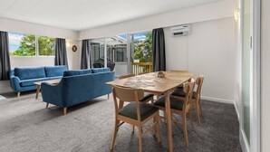 Ein modernes Wohnzimmer mit einem blauen Sofa, einem Holzesstisch mit Stühlen und einem großen Fenster mit Vorhängen.