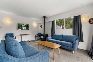 A modern living room with a blue sofa, a wooden coffee table, and a television mounted on the wall. - Amanda Lane - Snells Beach Holiday Home (Snells Beach)