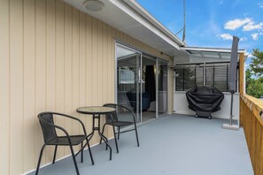 Un balcone con tavolo e due sedie, una porta scorrevole in vetro e un barbecue.