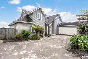 A two-story house with a garage, a driveway, and various plants. - Sunlit Shores - Papamoa Holiday Homes (Papamoa)