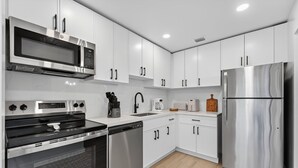 Une cuisine moderne dotée d’appareils électroménagers en acier inoxydable, de meubles blancs et d’un plancher en bois.