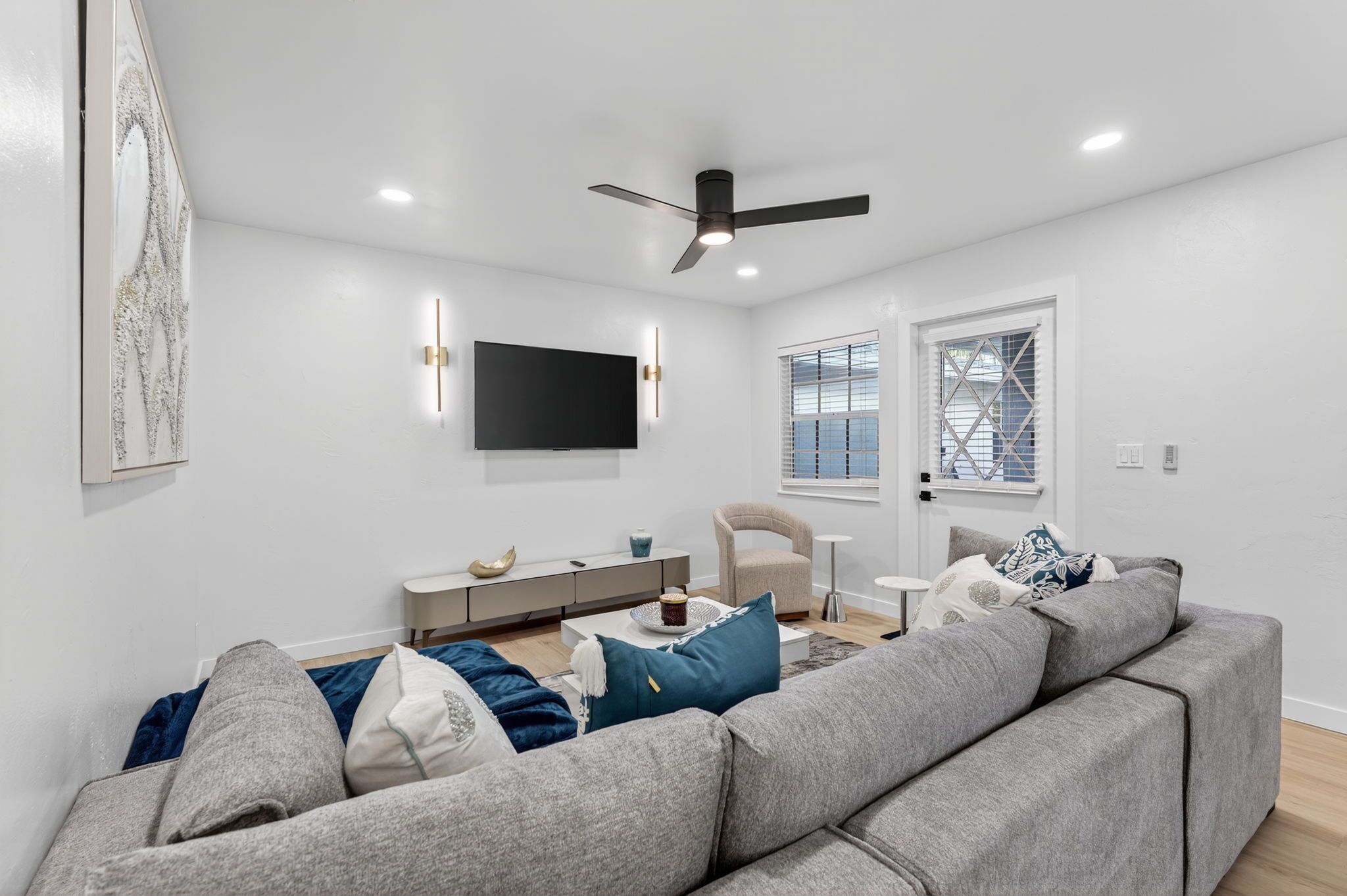 A modern living room with a grey sofa, a coffee table, a TV mounted on the wall, and a ceiling fan.