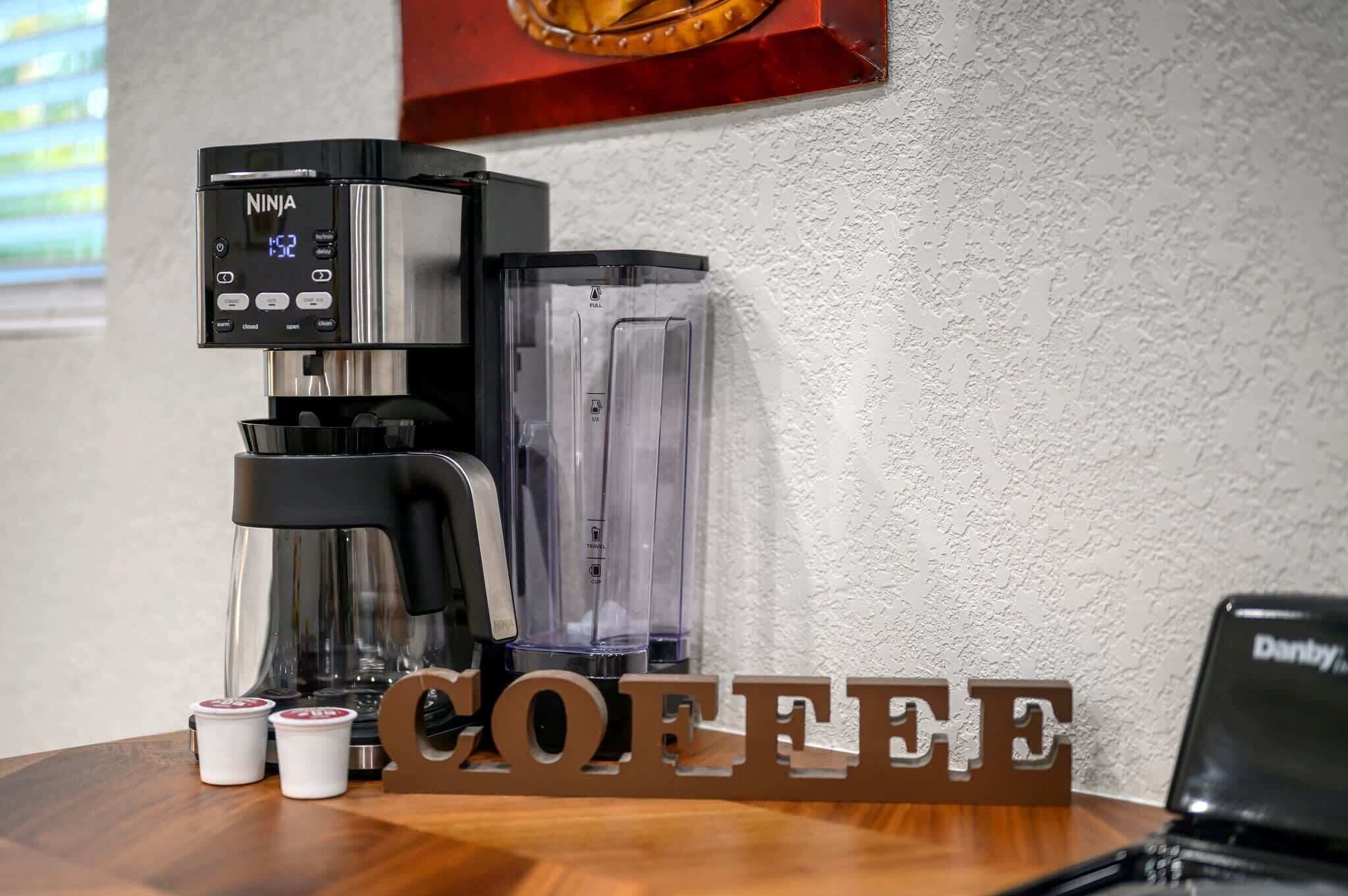 A coffee maker with a digital display, two small cups, and a wooden sign spelling "COFFEE" on a table.