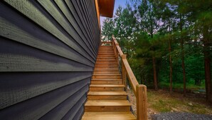 A wooden staircase leading up to a building with dark siding, surrounded by trees. - Double Magic - Unique Cabin for 6 - Pond, Hot Tub (Broken Bow)