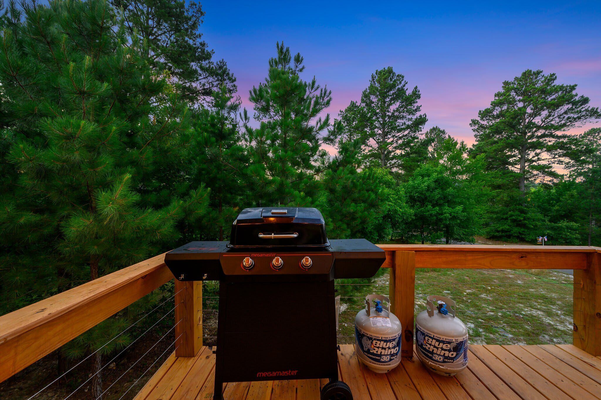 A barbecue grill on a wooden deck with a propane tank nearby.