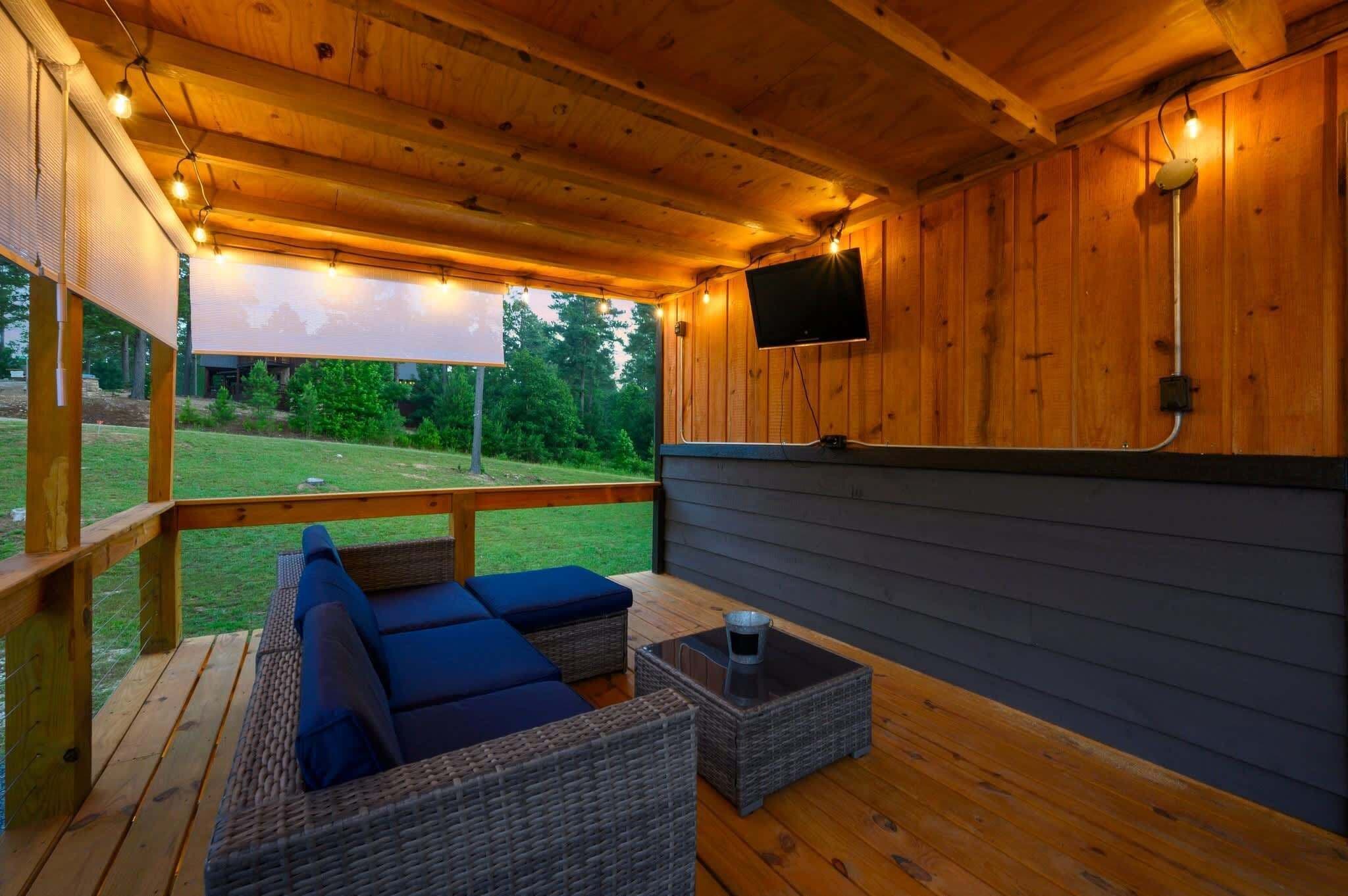 An outdoor deck with wicker furniture, a flat-screen TV, and string lights.