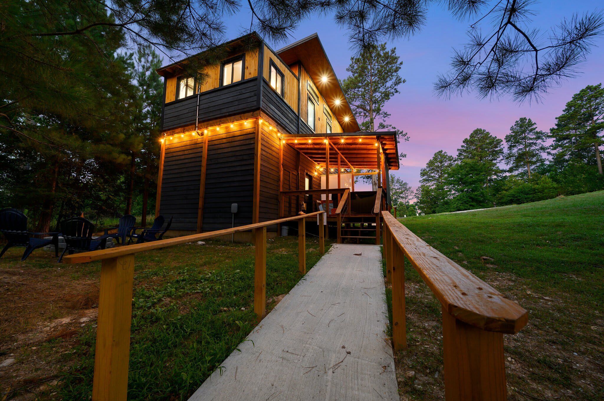 A wooden cabin with a porch and string lights, surrounded by trees.