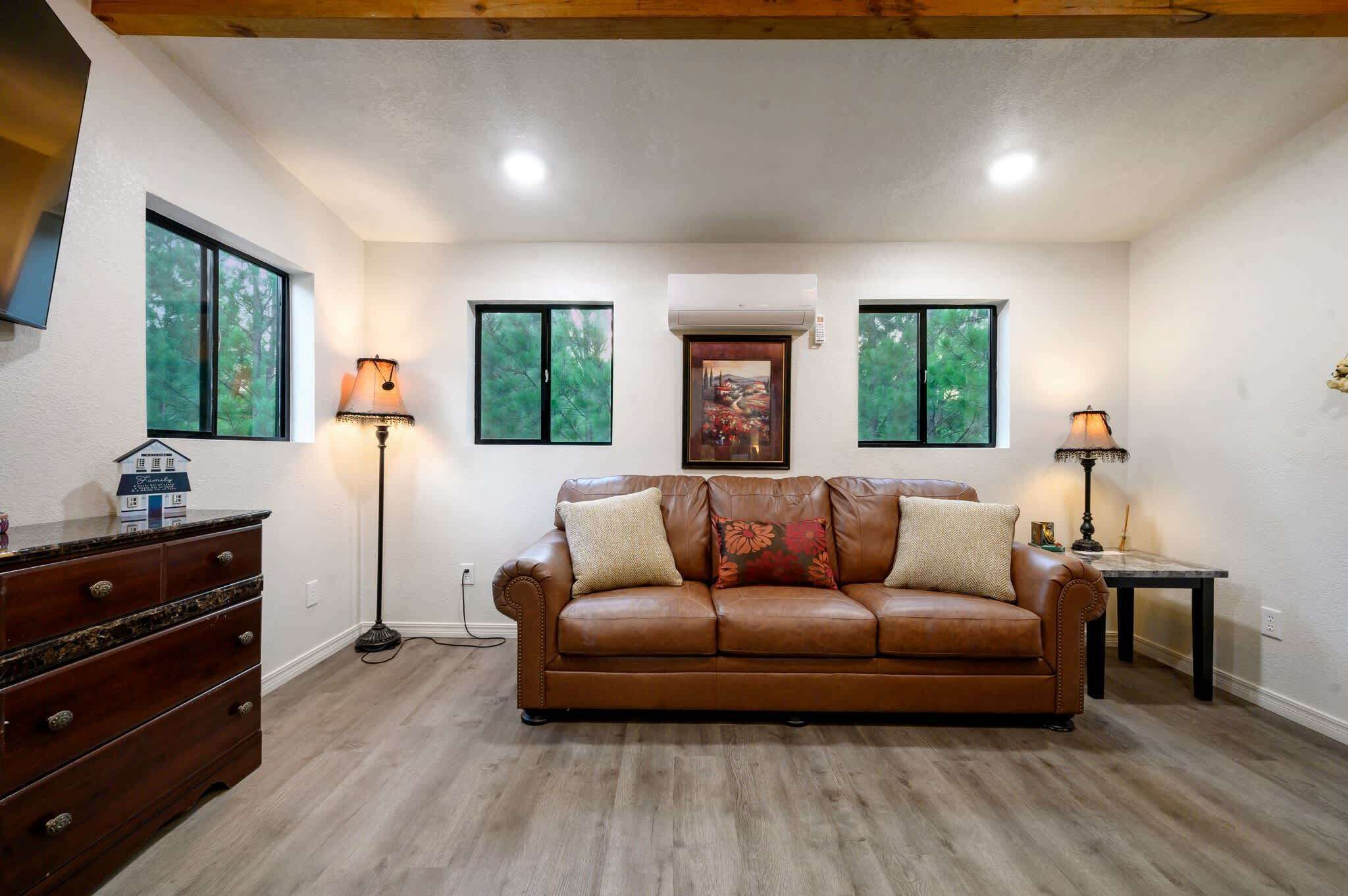 A living room with a brown leather sofa, two floor lamps, a wooden dresser, and a framed picture on the wall.