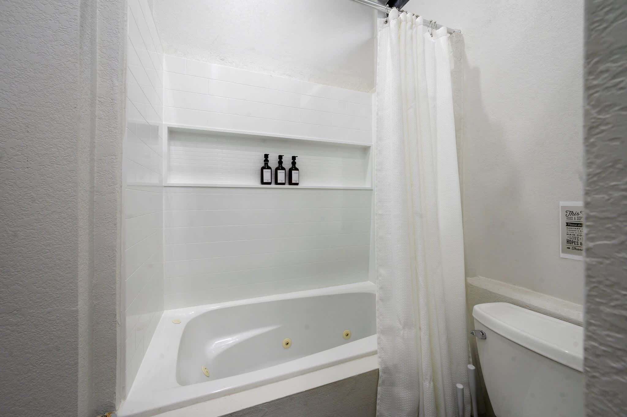 Une salle de bain avec une baignoire, des toilettes et une étagère remplie de bouteilles.