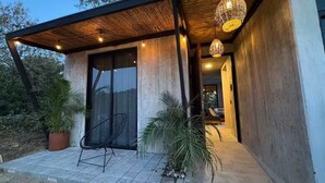 A modern building with a concrete exterior, a covered patio with a chair and potted plants, and hanging lights.