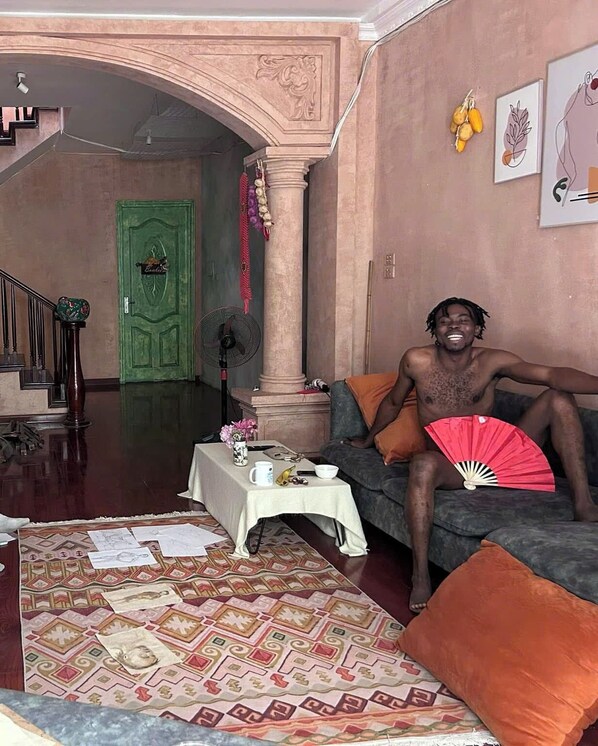Un salon comprenant un canapé, un ventilateur, une table avec un vase et un bol, ainsi qu’un tapis à motifs.