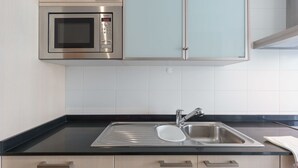 A kitchen with a built-in microwave, stainless steel sink, and light-colored cabinets. - Vilamourasun Aquamar 112 (Loulé)