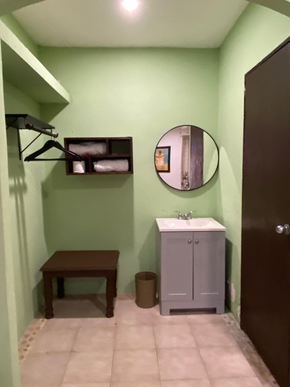 A bathroom with a sink, mirror, hanging clothes rack, and a small table.