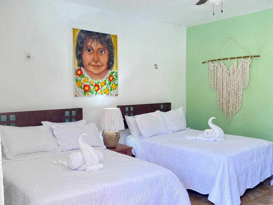 A room with two beds, a ceiling fan, a painting, and a macrame wall hanging.