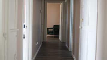 A hallway with a wooden floor and white walls. There are doors on both sides and a green chair in the distance.