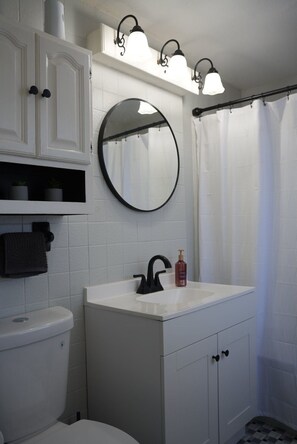 A bathroom with a white toilet, a round mirror, a black faucet, a white sink, and a shower curtain.
