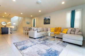 A modern living room with a sofa, coffee table, and a dining area. - Luxurious 6BR Home with Pool, BBQ & Game Room – Ideal for Families! (Kissimmee)