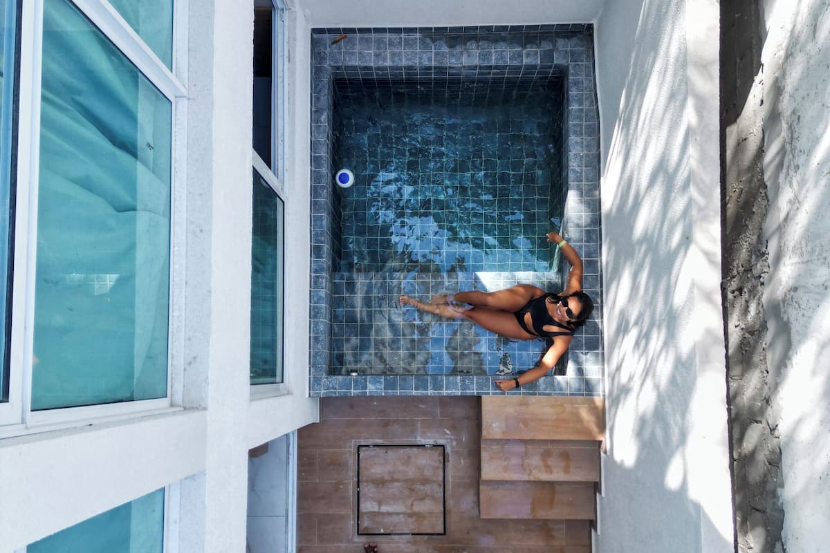 A rooftop pool with a tiled interior, a person swimming, and another person lying on the floor.