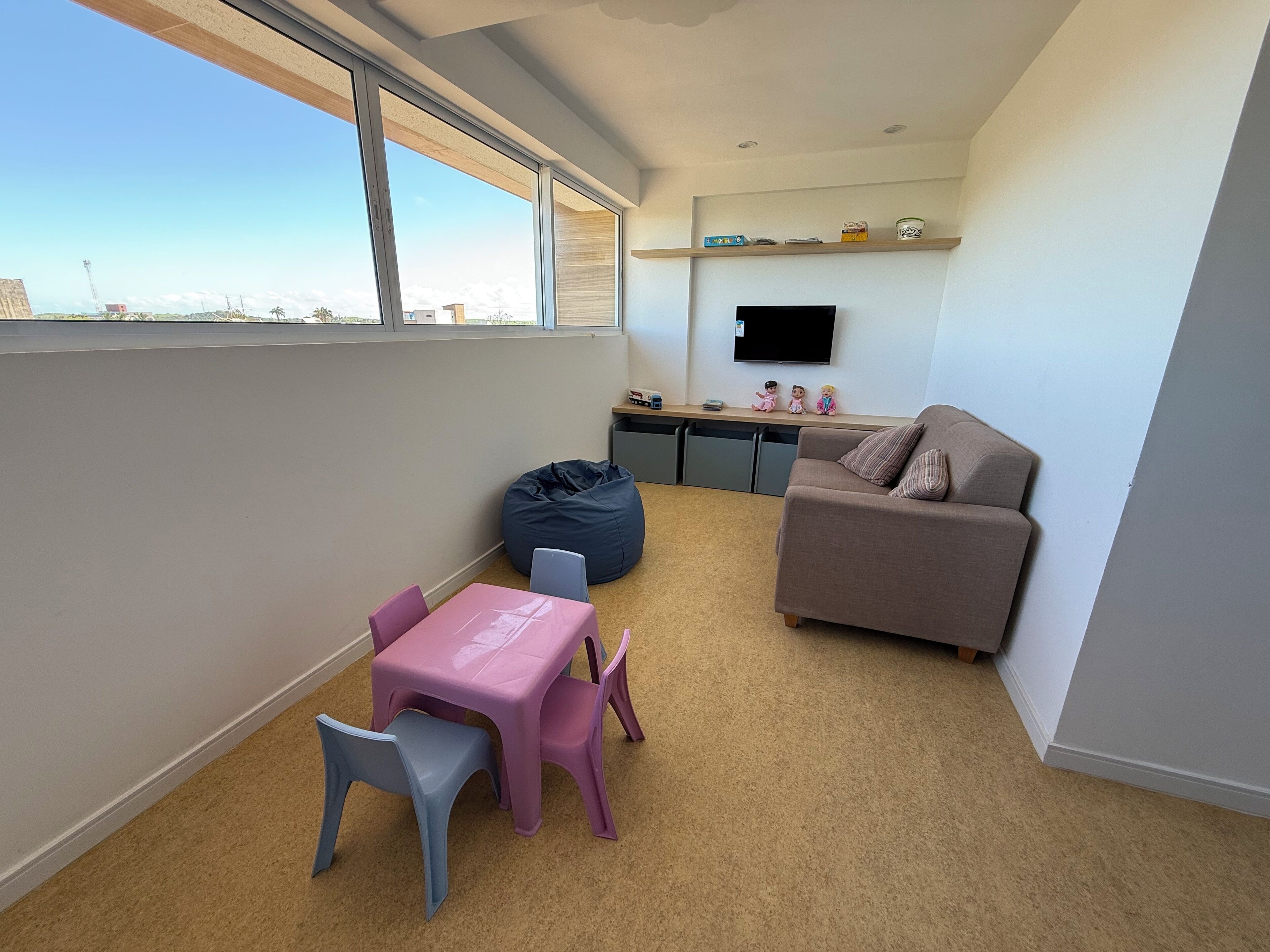 A modern apartment with a balcony, a kitchenette, a living area with a sofa and a TV, and a small table with chairs.