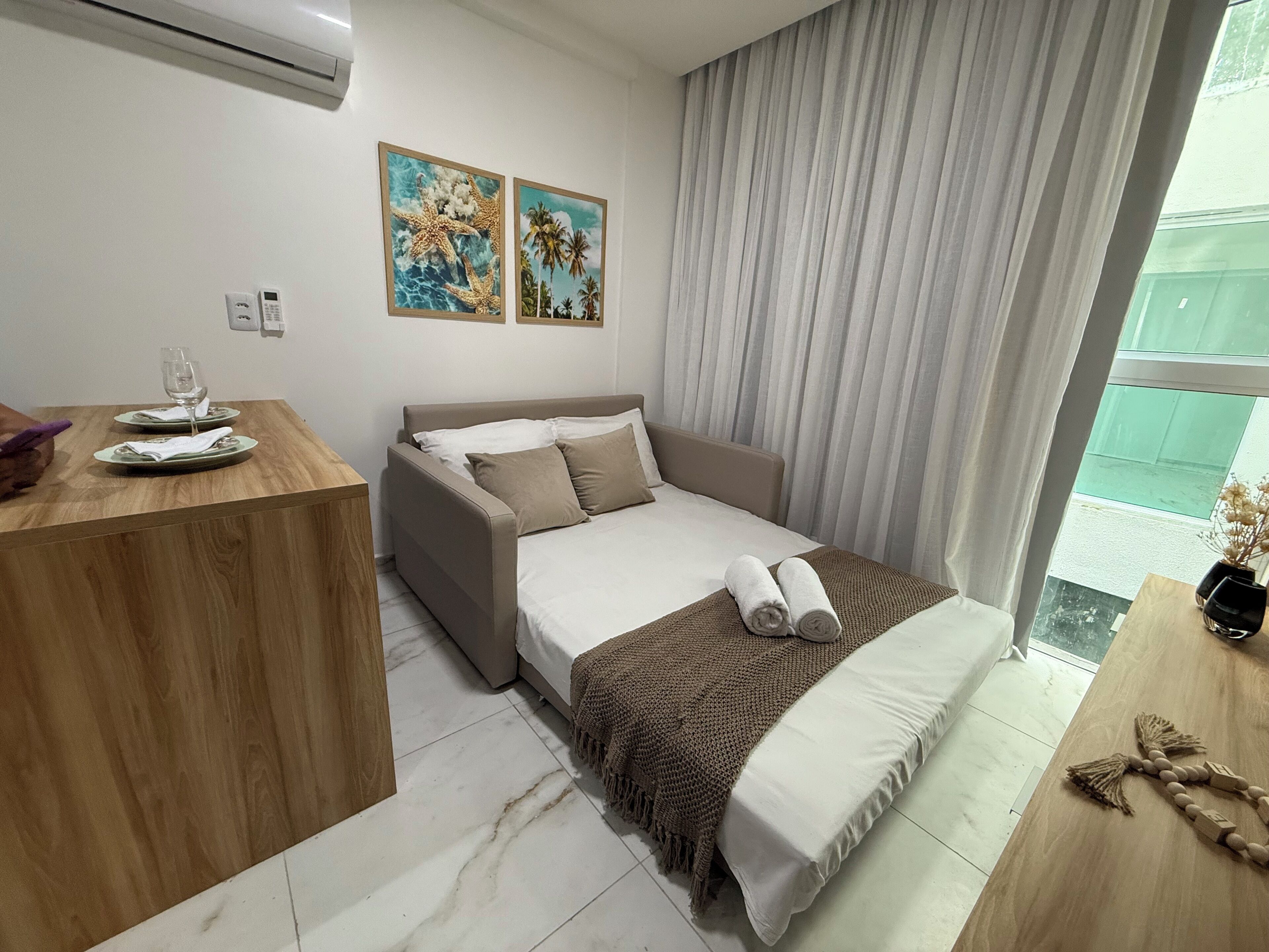 A modern hotel room with a bed, a wooden desk, and two framed pictures on the wall.