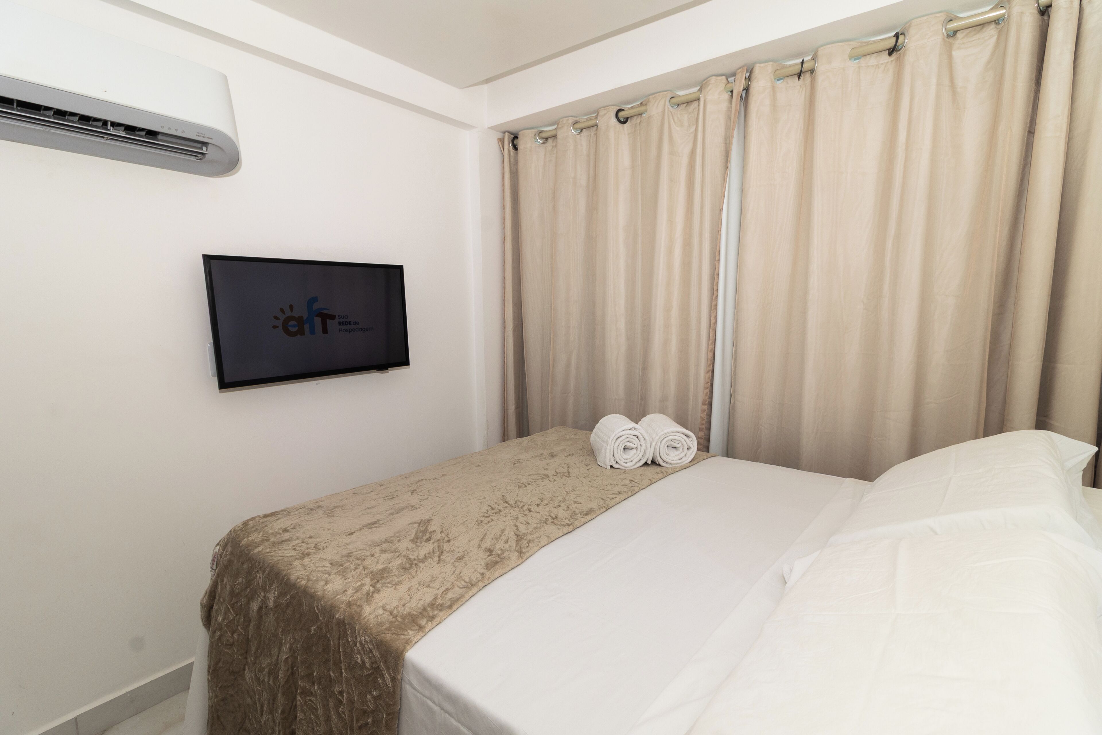 A hotel room with a bed, a TV mounted on the wall, and a window with curtains.