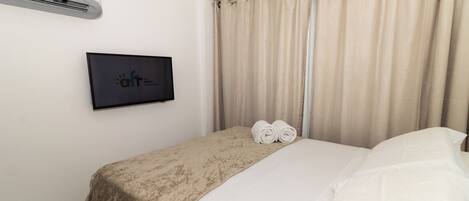 A hotel room with a bed, a TV mounted on the wall, and a window with curtains.