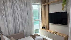 Egy modern szállodai szoba, amelyben található egy ágy, egy televízió, egy fa konzolasztal, és kilátás nyílik a szabadba.