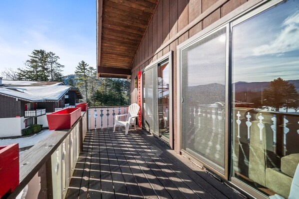 Eine Holzterrasse mit einer Glastür, die auf einen Balkon führt, ein weißer Stuhl und rote Pflanzgefäße.