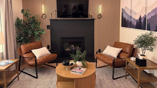 Een moderne woonkamer met twee leren fauteuils, een houten salontafel, een open haard en een grote televisie erboven bevestigd.
