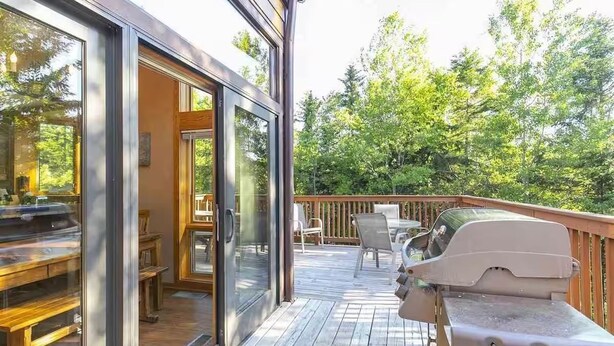 Eine Terrasse mit Grill, Gartenmöbeln und einer Glastür, die zu einem Innenbereich mit einem Klavier führt.