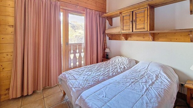 Un dormitori amb dos llits, parets de fusta, una finestra amb cortines i una prestatgeria de fusta sobre els llits.
