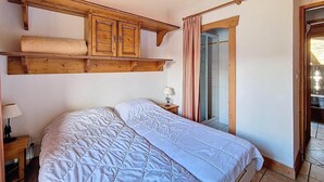 Un dormitori amb un llit gran, un capçal de fusta, una nitòria amb una làmpada i una finestra amb cortines.