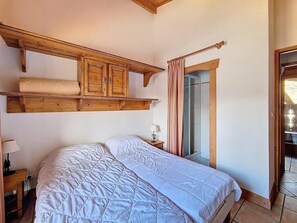 A bedroom with a large bed, wooden headboard, a nightstand with a lamp, and a window with curtains. - 100m from ski slopes, 2nd floor, swimming pool, tv, ski locker, 63m², Les Menuires (Les Menuires)